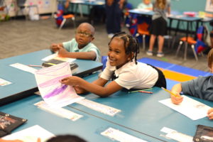 A little girl sharing her art with others in a classroom